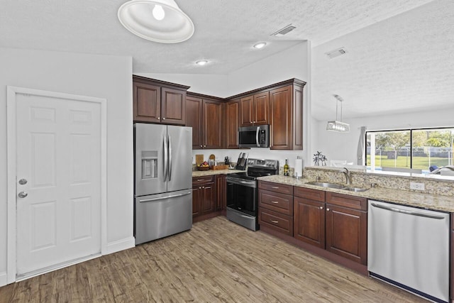 kitchen with sink, hanging light fixtures, light stone counters, light hardwood / wood-style floors, and stainless steel appliances