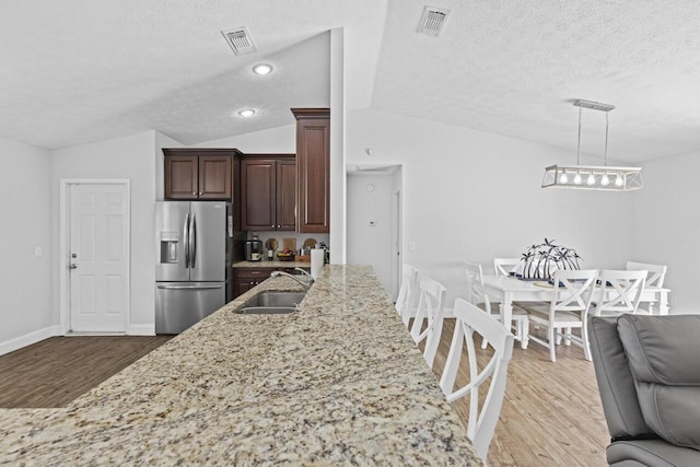 kitchen featuring decorative light fixtures, lofted ceiling, sink, light stone counters, and stainless steel fridge with ice dispenser