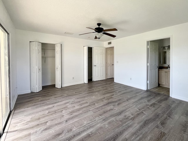 unfurnished bedroom with connected bathroom, light wood-type flooring, ceiling fan, multiple closets, and a textured ceiling