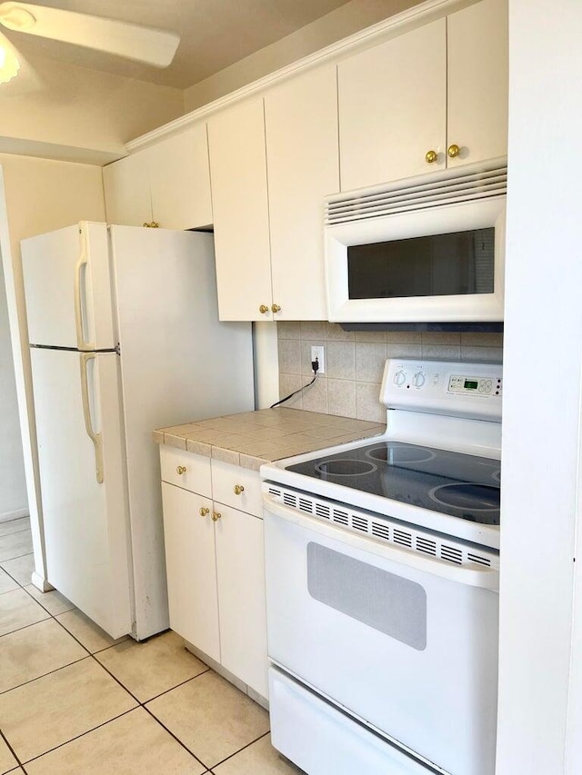 kitchen with tasteful backsplash, white appliances, light tile patterned flooring, and white cabinets