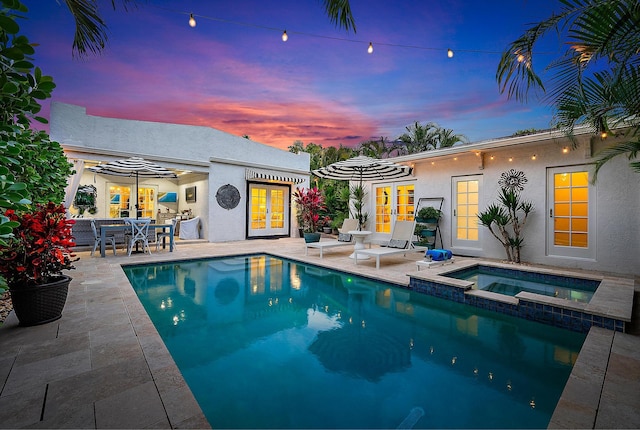 pool at dusk featuring an in ground hot tub, a patio area, and french doors