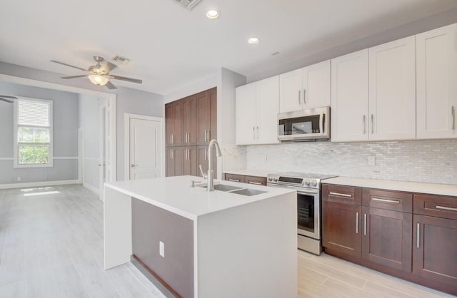 kitchen with sink, white cabinetry, an island with sink, stainless steel appliances, and backsplash