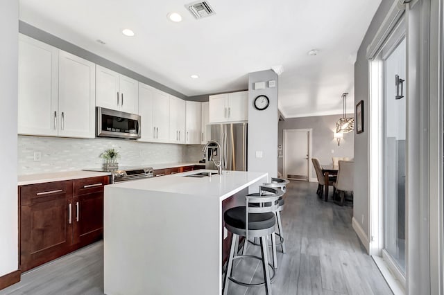 kitchen with sink, a breakfast bar area, a center island with sink, stainless steel appliances, and backsplash