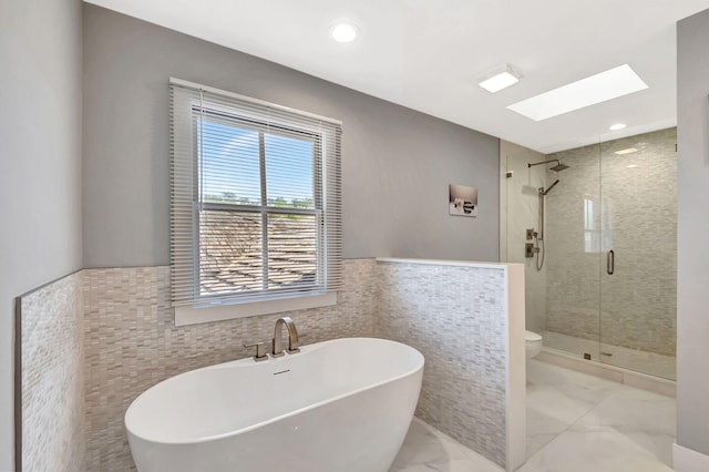 bathroom featuring separate shower and tub, toilet, a skylight, and tile walls