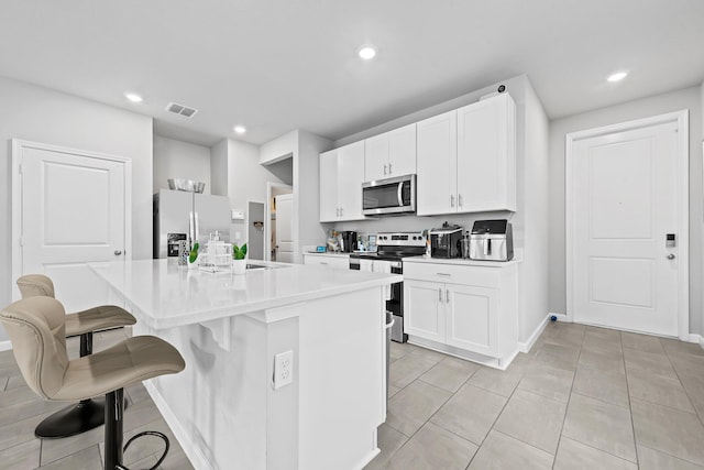 kitchen featuring stainless steel appliances, white cabinetry, a kitchen island with sink, and a kitchen bar