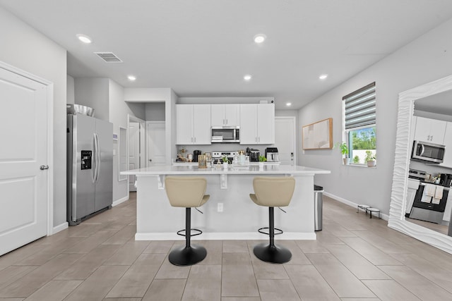 kitchen with an island with sink, appliances with stainless steel finishes, a breakfast bar area, and white cabinets