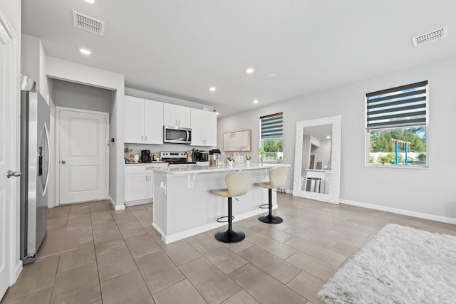 kitchen featuring stainless steel appliances, a kitchen breakfast bar, an island with sink, a healthy amount of sunlight, and white cabinets