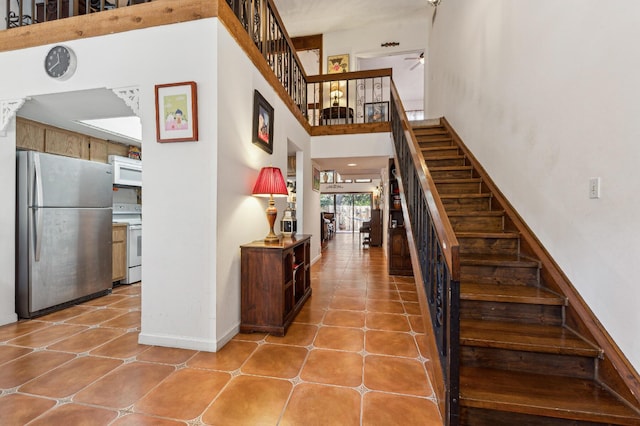 stairway with a towering ceiling, tile patterned floors, and ceiling fan