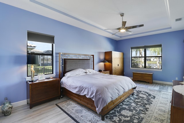 bedroom featuring a tray ceiling, ceiling fan, and light wood-type flooring