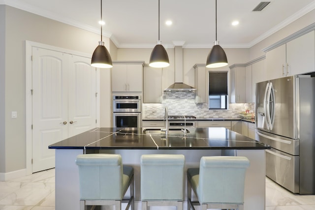 kitchen with decorative light fixtures, an island with sink, wall chimney exhaust hood, and appliances with stainless steel finishes