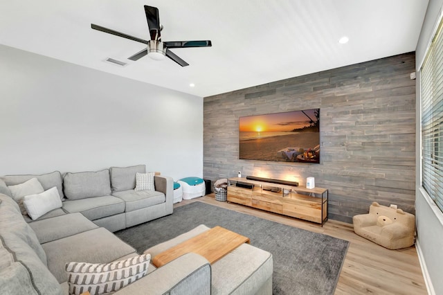 living room with wood walls, ceiling fan, and light hardwood / wood-style flooring