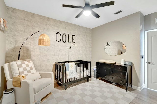 bedroom featuring light hardwood / wood-style flooring, a nursery area, and ceiling fan