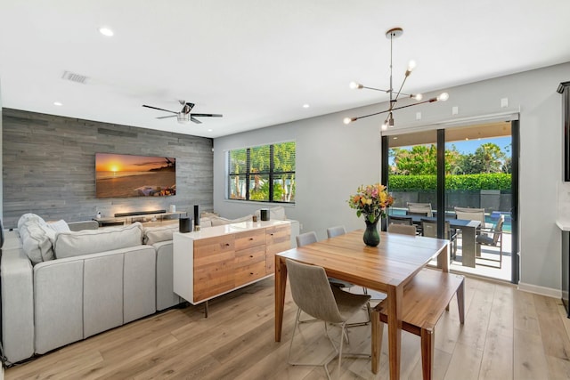 dining space featuring ceiling fan with notable chandelier, wooden walls, a healthy amount of sunlight, and light wood-type flooring