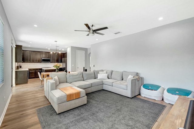 living room with sink, ceiling fan with notable chandelier, and light wood-type flooring