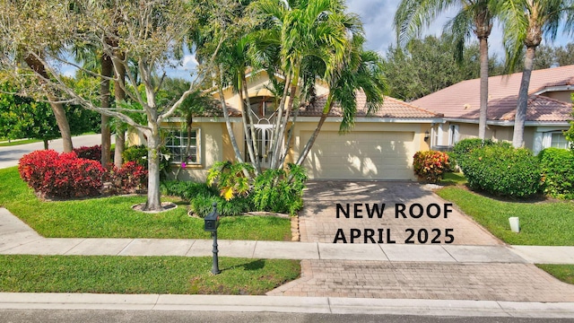 view of front of property with stucco siding, driveway, a front yard, an attached garage, and a tiled roof