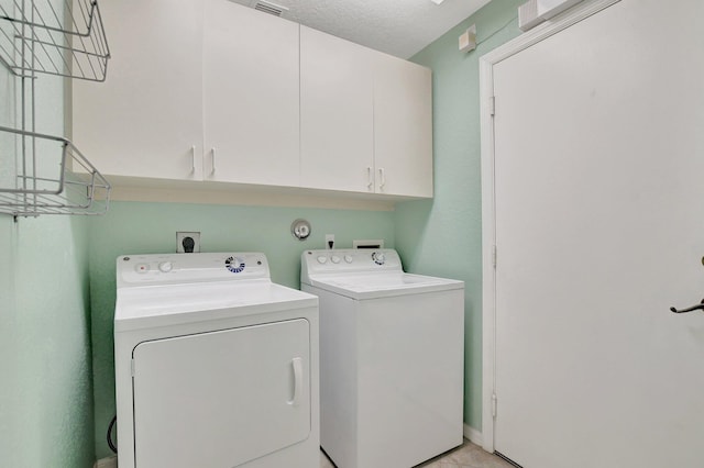 clothes washing area with cabinets, a textured ceiling, and washing machine and clothes dryer