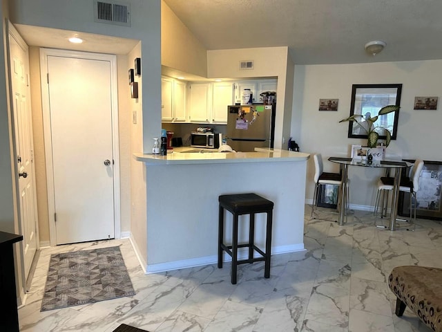 kitchen featuring a breakfast bar area, appliances with stainless steel finishes, white cabinets, vaulted ceiling, and kitchen peninsula