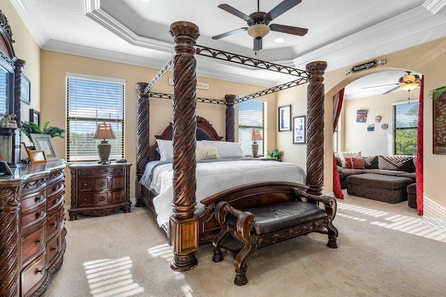 carpeted bedroom featuring decorative columns, ornamental molding, ceiling fan, and a tray ceiling