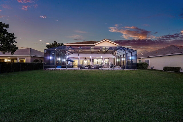 back house at dusk with a lanai, a lawn, and a patio