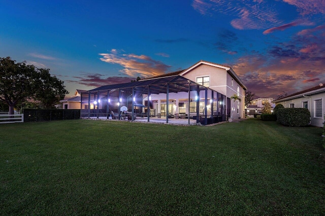 back house at dusk with a lanai and a lawn