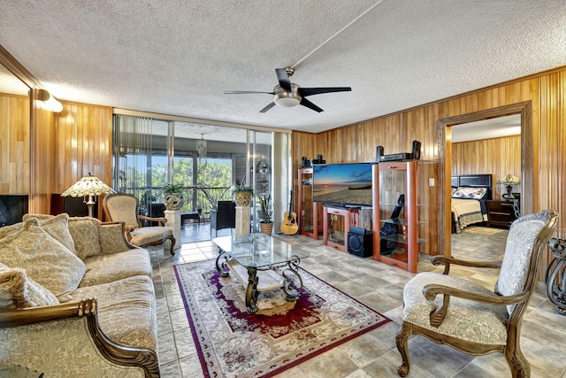 living room featuring wood walls, ornamental molding, ceiling fan, a barn door, and a textured ceiling