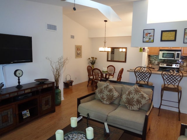 living room featuring vaulted ceiling with skylight and light wood-type flooring