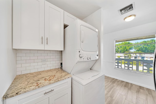 laundry area with visible vents, cabinet space, stacked washer and clothes dryer, and baseboards