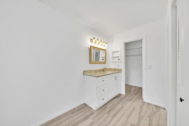 bathroom featuring baseboards, a walk in closet, wood finished floors, and vanity