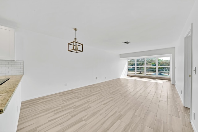 unfurnished living room with an inviting chandelier, light wood-style flooring, visible vents, and baseboards