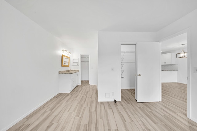 unfurnished bedroom with light wood-type flooring, baseboards, a walk in closet, and a closet