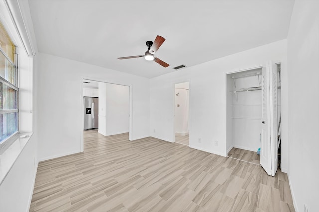 unfurnished bedroom with a ceiling fan, baseboards, visible vents, light wood-type flooring, and stainless steel fridge with ice dispenser