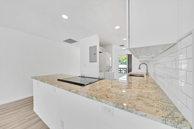 kitchen featuring a sink, white cabinets, stacked washing maching and dryer, backsplash, and light stone countertops