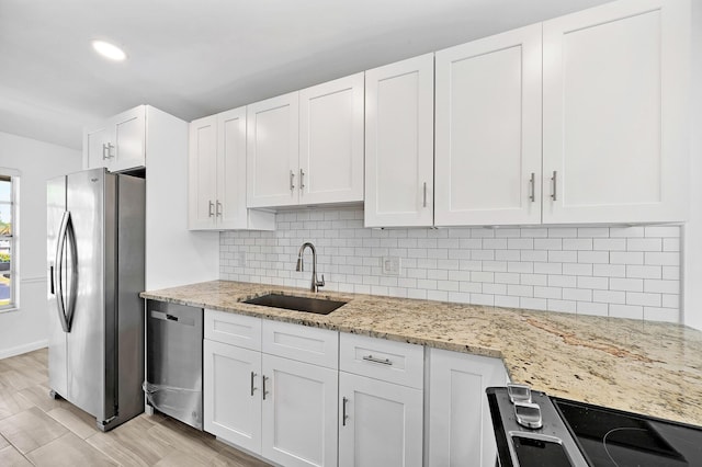 kitchen featuring light stone counters, a sink, white cabinets, appliances with stainless steel finishes, and backsplash