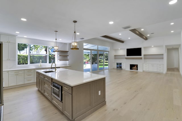 kitchen featuring sink, stainless steel oven, hanging light fixtures, a kitchen island with sink, and white cabinets