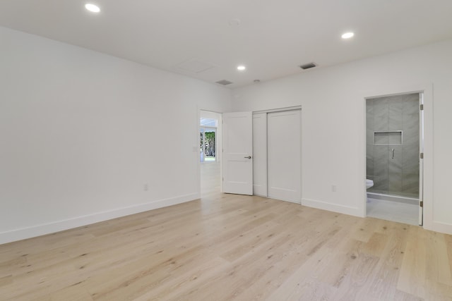 unfurnished bedroom featuring ensuite bath, a closet, and light wood-type flooring