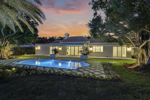 pool at dusk featuring a lawn and a patio