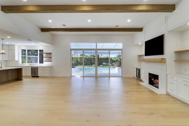 unfurnished living room with sink, beam ceiling, and light hardwood / wood-style floors