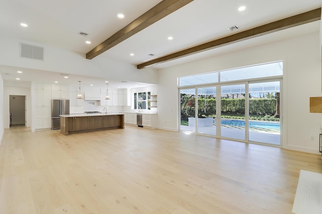 unfurnished living room featuring beamed ceiling, sink, and light wood-type flooring