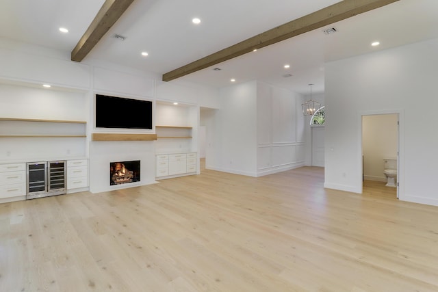 unfurnished living room featuring wine cooler, beam ceiling, a chandelier, and light hardwood / wood-style floors