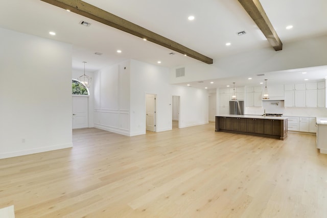 unfurnished living room with a notable chandelier, beam ceiling, and light hardwood / wood-style flooring