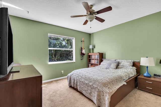 bedroom featuring light carpet, ceiling fan, baseboards, and a textured ceiling