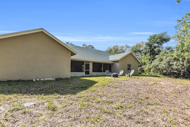 back of house with a fire pit, a shingled roof, a sunroom, and stucco siding