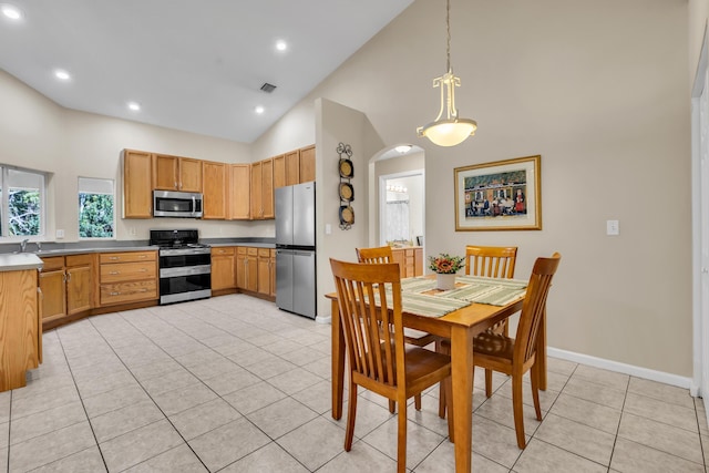 kitchen featuring arched walkways, hanging light fixtures, appliances with stainless steel finishes, light tile patterned flooring, and baseboards