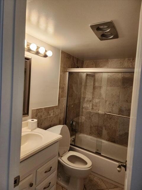 full bathroom with tile walls, bath / shower combo with glass door, vanity, tile patterned floors, and toilet