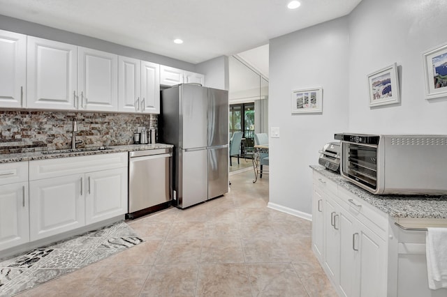 kitchen with sink, white cabinets, decorative backsplash, stainless steel appliances, and light stone countertops