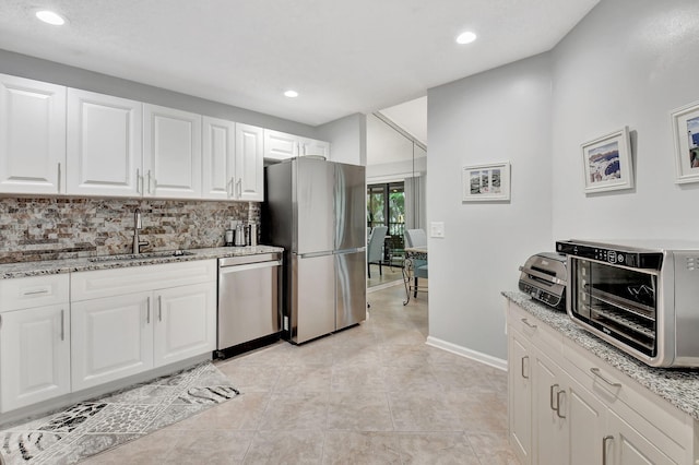 kitchen featuring appliances with stainless steel finishes, tasteful backsplash, sink, white cabinets, and light stone counters