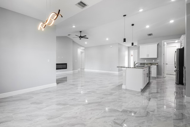 kitchen with pendant lighting, stainless steel fridge, an island with sink, and white cabinets