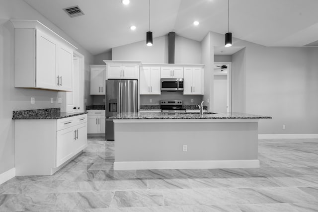 kitchen featuring appliances with stainless steel finishes, decorative light fixtures, an island with sink, dark stone countertops, and white cabinets