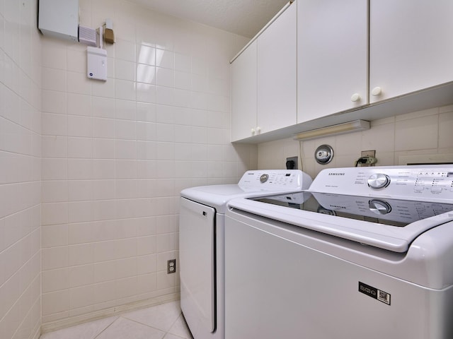 laundry room featuring tile walls, washer and clothes dryer, cabinets, and light tile patterned flooring