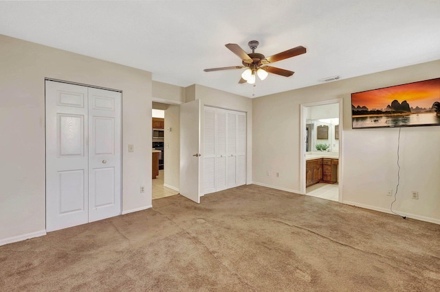 unfurnished bedroom with light carpet, two closets, ceiling fan, and ensuite bathroom